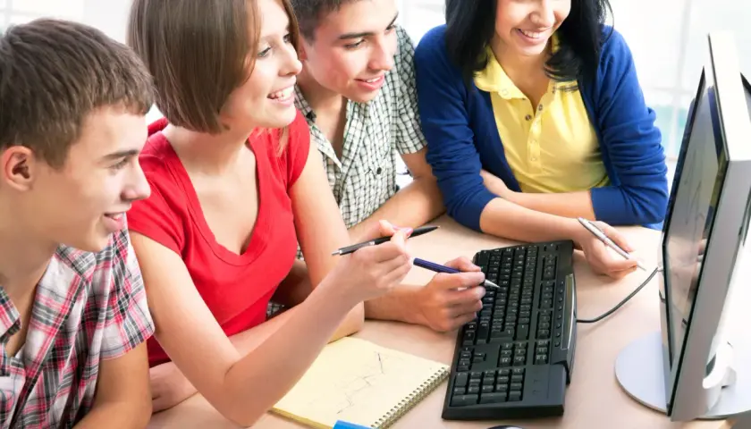 Vier junge Leute arbeiten an einem Computer. Sie sind engagiert und lachen, was auf gute Gruppenarbeiten Ideen für Erwachsene hindeutet.
