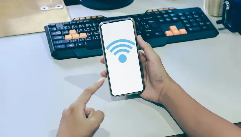 Dłoń trzyma smartfon z ikoną Wi-Fi. Dowiedz się, jak sprawdzić częstotliwość Wi-Fi w telefonie, aby zoptymalizować połączenie.