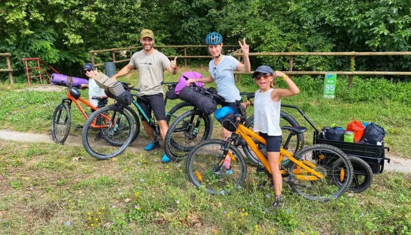 Familia lista para la ruta Pirinexus, con bicicletas y equipaje, disfrutando del paisaje verde.