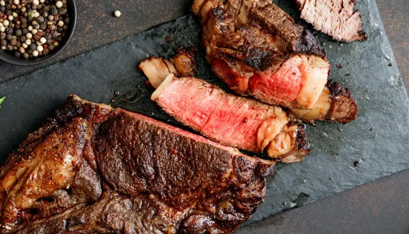 Un steak de bœuf juteux, coupé en tranches, révèle une cuisson parfaite grâce à la méthode de cuisson reverse sear. Poivre noir et blanc en accompagnement.