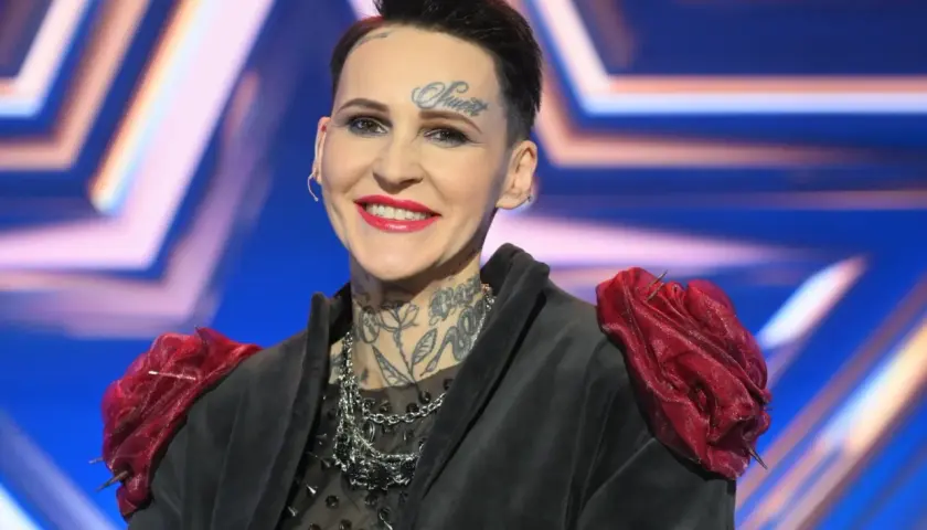 Agnieszka Chylińska z tatuażami na twarzy i szyi, w czarnej marynarce z czerwonymi ozdobami na ramionach.