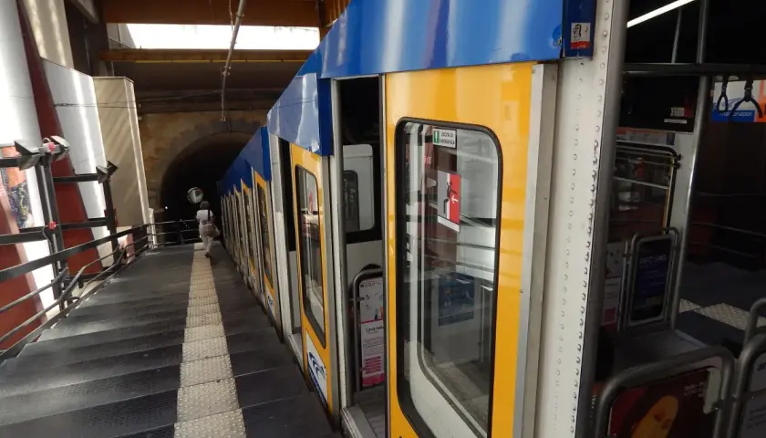 Żółto-niebieski wagonik metra neapol stoi na peronie, obok schodów prowadzących do tunelu.