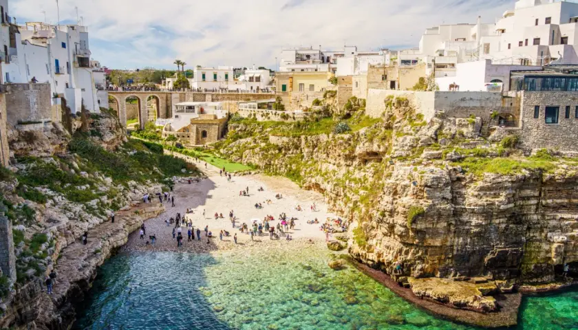 Malownicze klify i białe domy Polignano a Mare, z plażą pełną ludzi i turkusową wodą.