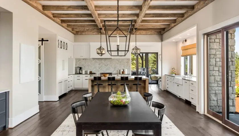 Comedor y cocina de estilo farmhouse con vigas de madera expuestas, isla central con taburetes y mesa oscura.