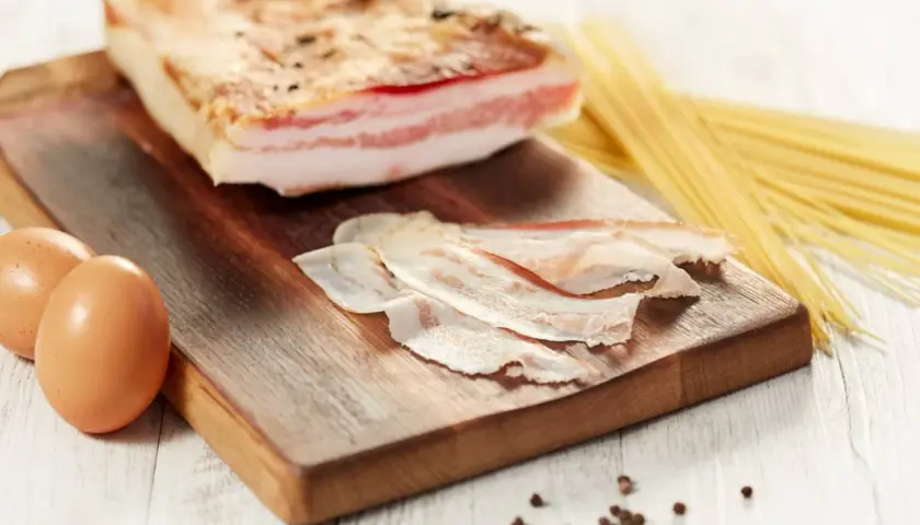 Ingredienti per una pasta con guanciale perfetta: un pezzo di guanciale, uova e spaghetti.
