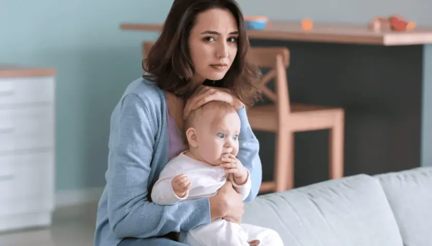 Smutna młoda mama tuli dziecko, czując się przytłoczona. To może być depresja w ciąży, która dotyka wiele kobiet.