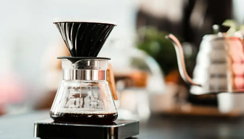 Kaffee tropft in eine Glaskaraffe, während sich der blooming effekt entfaltet. Im Hintergrund eine Kaffeekanne.