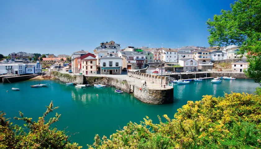 El pintoresco puerto vega, con sus casas coloridas y barcos meciéndose en aguas turquesas, bajo un cielo azul.