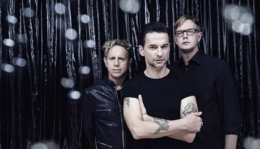 Skład Depeche Mode: Martin Gore, Dave Gahan i Andy Fletcher pozują na tle błyszczącej, czarnej kurtyny.