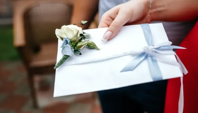 Biała koperta z błękitną wstążką i butonierką. Zastanawiasz się, ile chrzestny daje na wesele?