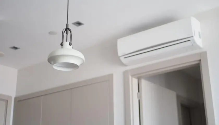 Biały klimatyzator ścienny nad drzwiami, obok lampy wiszącej.