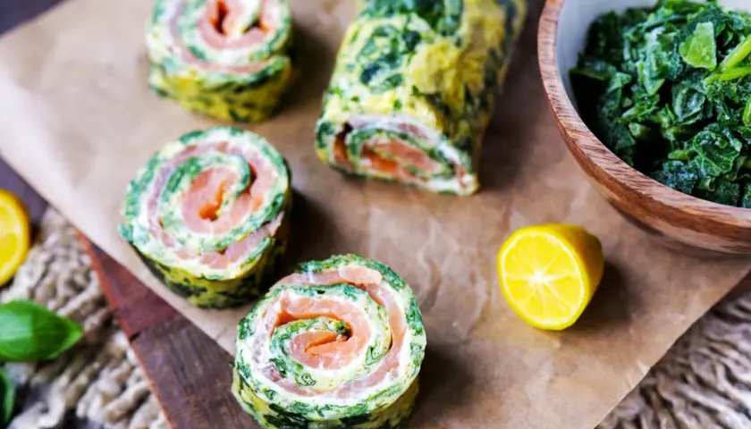 Spinat-Lachs-Röllchen, eine köstliche low carb Mahlzeit. Serviert mit frischem Spinat und Zitrone.