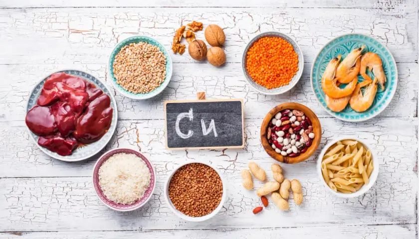 Na tabliczce napisano "Cu". Wokół niej są produkty bogate w miedź: wątróbka, soczewica, fasola, orzechy, krewetki, ryż, kasza gryczana, pszenica, makaron i orzeszki ziemne. Czy miedź rdzewieje? Nie, ale jest niezbędna dla zdrowia.