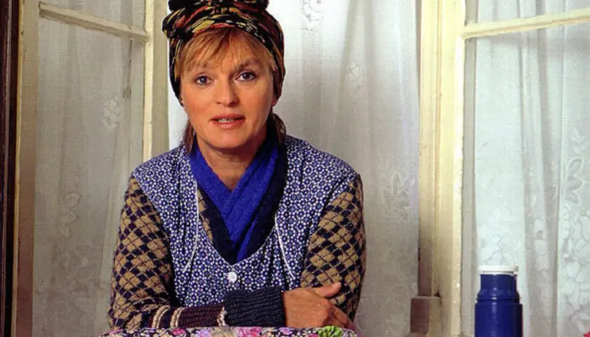 Else Stratmann sitzt am Fenster, eine bunte Kopftuch ziert ihr Haar. Sie trägt eine blaue Bluse mit weißen Punkten und eine Strickjacke.