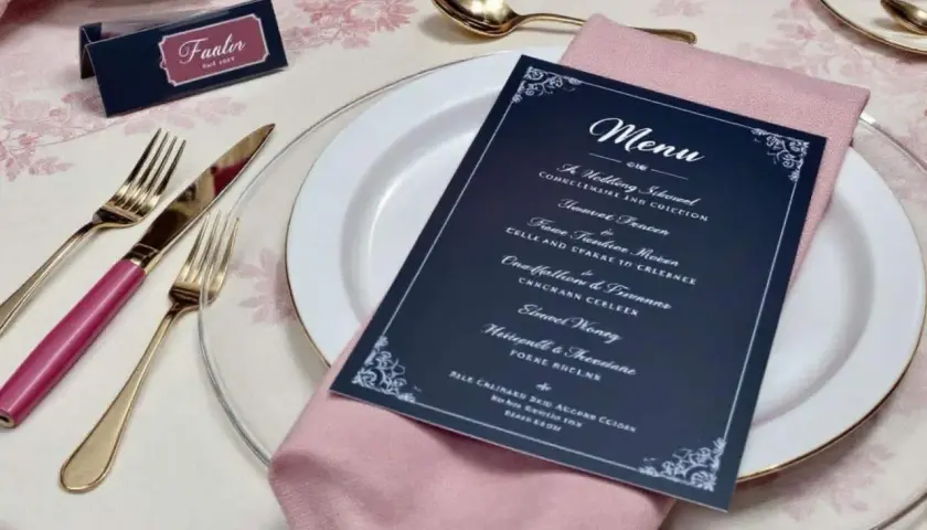 Une table dressée pour un mariage, avec une carte de menu originale, des couverts dorés et une serviette rose.
