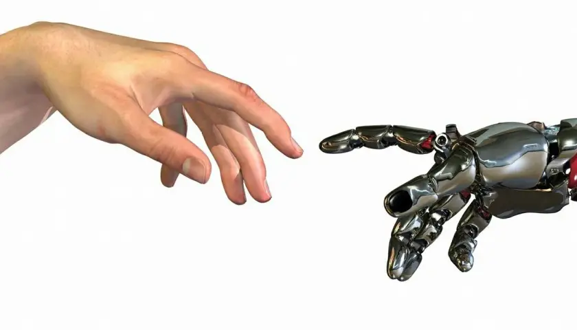 Ludzka dłoń i mechaniczna ręka zbliżają się do siebie, niemal dotykając. To symboliczny touche między człowiekiem a technologią.