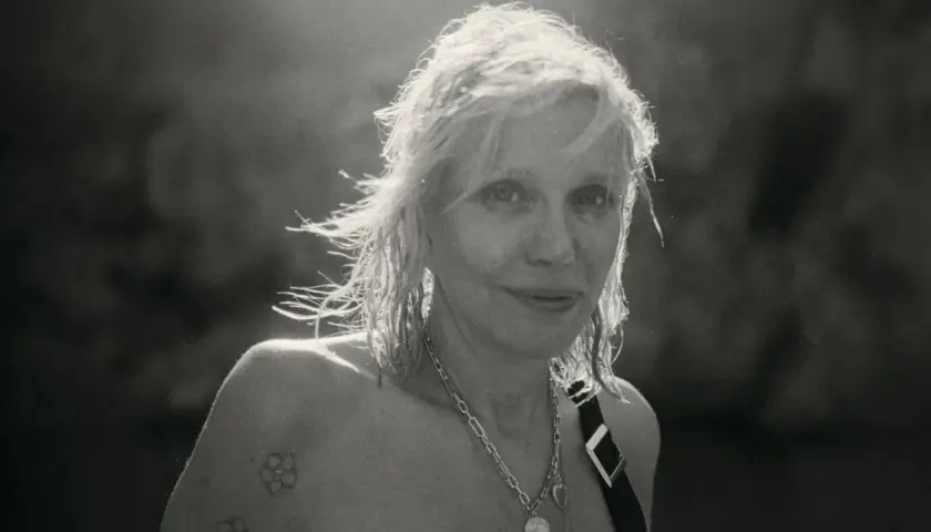 Courtney Love, ikona grunge, z rozwianymi włosami i tatuażem na ramieniu, emanuje siłą.
