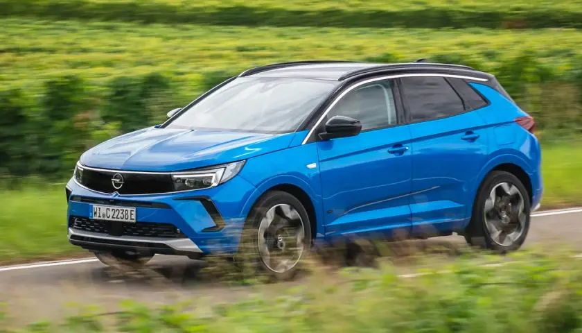 Blå Opel Grandland kör på en landsväg, omgiven av suddiga gröna fält. Kanske ett opel grandland problem med att hålla sig på vägen?