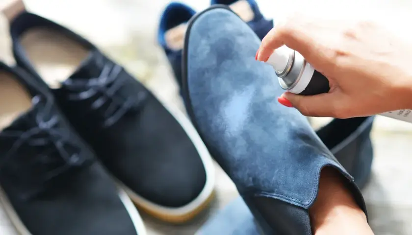 Aplicando spray protector a unas botas de terciopelo azul. Aprende como limpiar botas de terciopelo para mantenerlas como nuevas.
