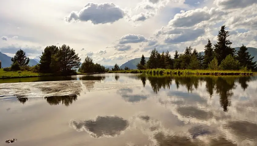 La bassa d'Arres, un espejo de agua sereno, refleja árboles frondosos y un cielo nublado.