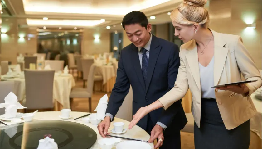 Ein Mann und eine Frau richten einen Tisch in einem Restaurant für ein Event her. Sie besprechen Details, die für das eventmanager gehalt wichtig sind.