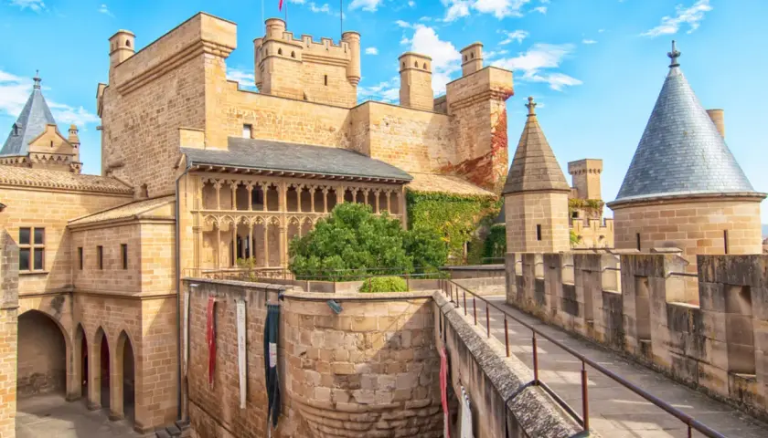 Imponente fortaleza de los castillos de España, con torres cónicas y un patio bajo un cielo azul y nubes blancas.