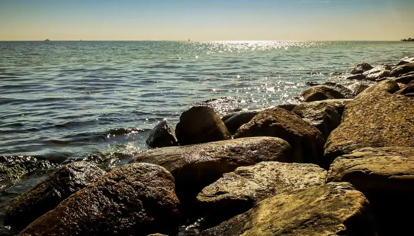 Kamienista plaża, fale rozbijające się o brzeg. W oddali widać statki i horyzont. Idealne miejsce na spacer w miejscowościach obok Ustki.