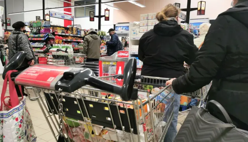 Ludzie robią zakupy w supermarkecie, zastanawiając się, czy w Wielką Sobotę można pracować. Wózek sklepowy pełen produktów.