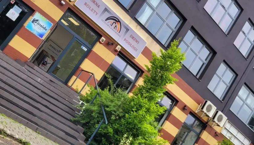 Elegancki budynek z oknami i drzwiami, z zielenią przed wejściem.