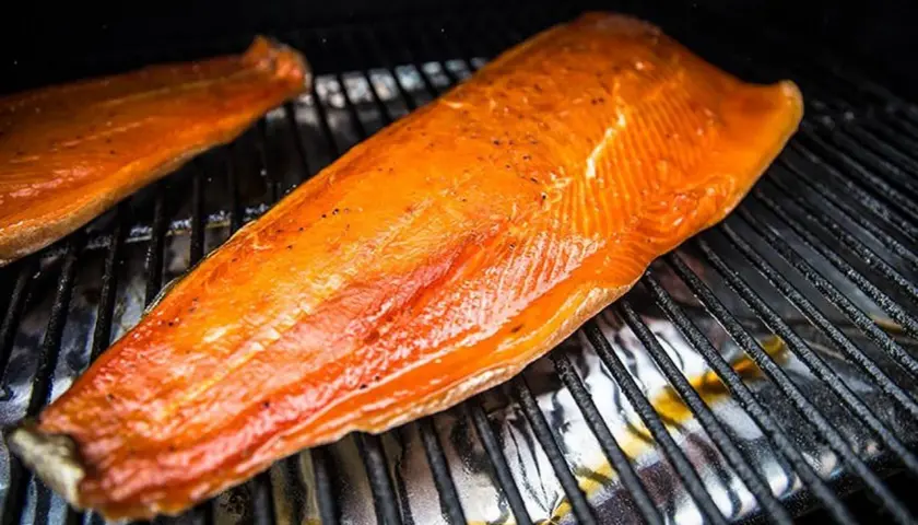 Deux filets de saumon orangés, assaisonnés de poivre, reposent sur une grille. Le temps de fumage à froid est presque terminé.