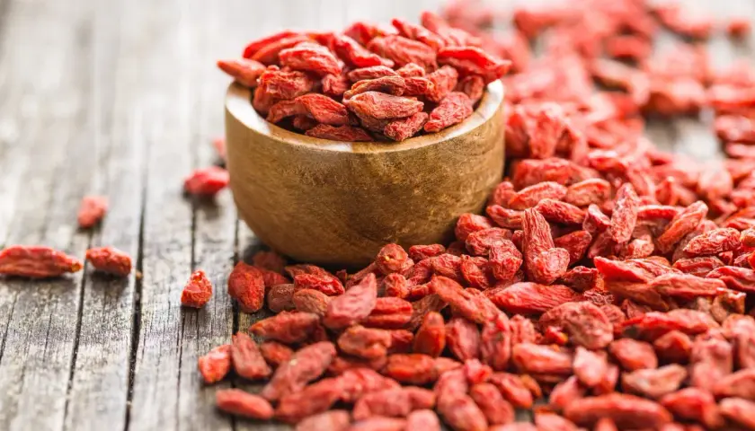 Suszone jagody goji rozsypane wokół drewnianej miseczki. Idealne do deserów, smoothie i jako zdrowa przekąska.
