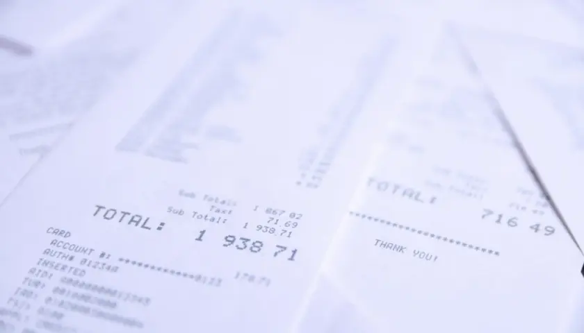 Stosy paragonów z widocznym napisem "TOTAL". Jeden z nich pokazuje kwotę 1 938,71, inny 716,49. Wsto oss.