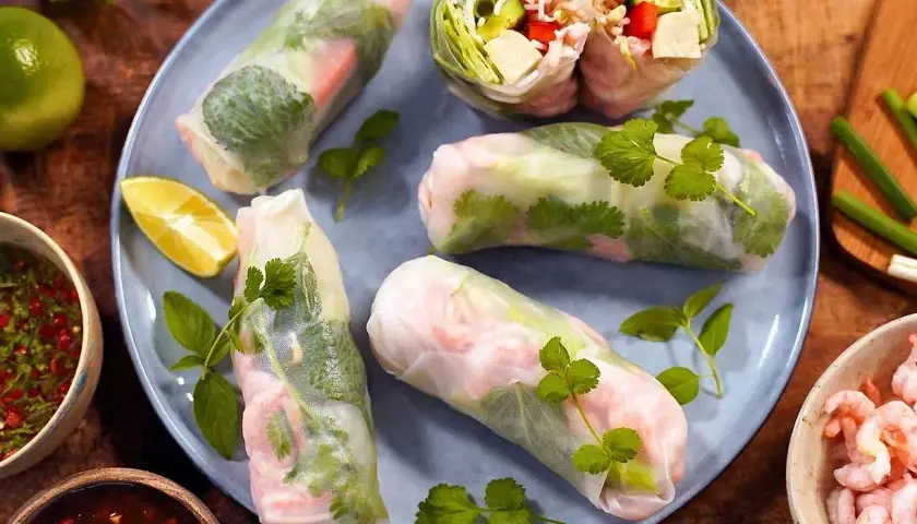 Färska sommarrullar med räkor och grönsaker, serverade med en smakrik vietnamesisk sås och limeklyftor.