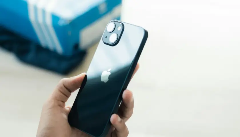 Dłoń trzyma ciemny iPhone 13, zastanawiając się, czy iPhone 13 jest wodoszczelny. W tle niebieskie pudełko.