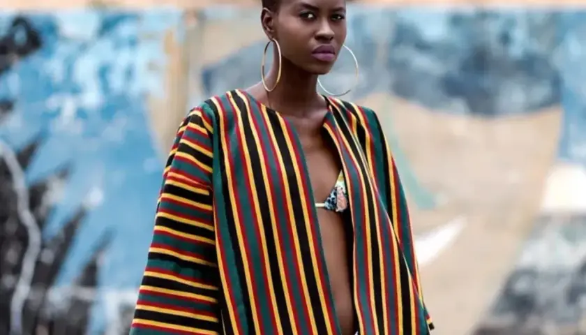 A woman models a vibrant Ankara fabric jacket with bold stripes of red, yellow, green, and black.