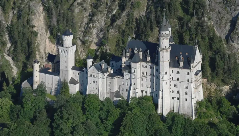 Bajkowy zamek w Niemczech, Neuschwanstein, wyrasta z zielonych lasów na tle skalistego zbocza.