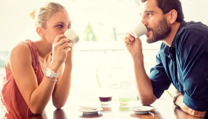 Coppia al bar, lui la guarda intensamente, un uomo innamorato in segreto che cerca il suo sguardo mentre bevono un caffè.