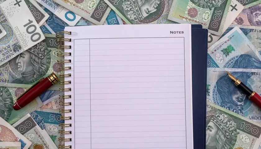 Notatnik i długopis na stosie polskich banknotów. Czy to miejsce na zapisanie, ile zarabia przewodniczący rady miasta?