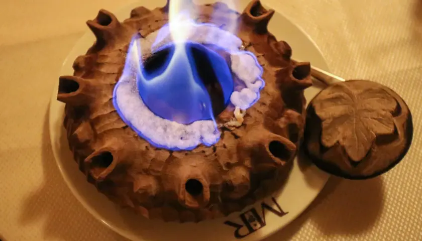 Caffè alla Valdostana in fiamme, servito in una coppa di terracotta con un coperchio intagliato.