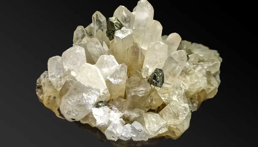 Ein Cluster aus klaren Quarzkristallen mit eingelagerten dunklen Mineralien. Die Quarz-Bedeutung liegt in seiner Klarheit und Reinheit, die oft mit Energie und Heilung assoziiert wird.