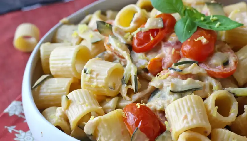 Piatto cremoso di pasta con zucchine, pomodorini e un tocco di Philadelphia, guarnito con basilico fresco.
