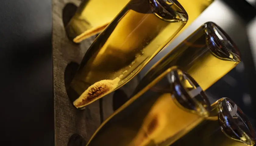 Flaschen mit goldgelbem Inhalt, vielleicht ein cremiger Wein oder ein süßer Likör. Die Sedimente am Flaschenboden deuten auf eine traditionelle Herstellung hin.