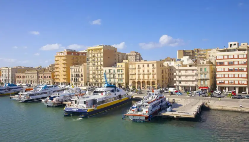 Ferries docked in a harbor, with buildings lining the waterfront. Wondering if you can drive to Sicily? These ferries might be your answer!