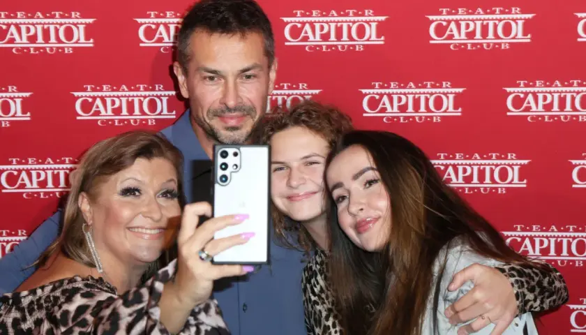 Katarzyna Skrzynecka z rodziną robi selfie. Uśmiechnięci rodzice i ich dzieci pozują na tle czerwonego banera z napisem "Teatr Capitol".