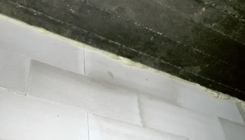 Piana montażowa wypełnia szczelinę między betonowym stropem a ścianą z białych pustaków. Idealne rozwiązanie, czym wypełnić dylatacje w ścianie.