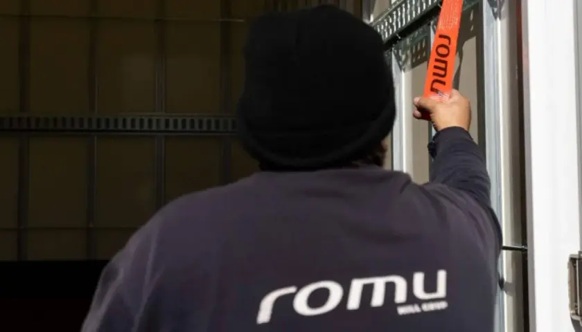 Persona con gorro negro asegura trincajes de cargas con una cinta naranja de la marca Romu.