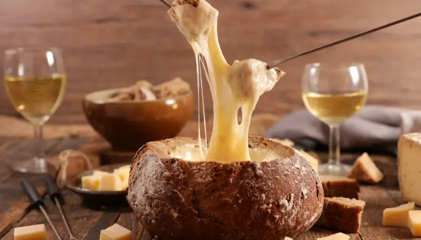 Un pain creusé sert de bol pour une fondue au vin blanc dégoulinante. Des morceaux de pain et de fromage sont prêts à être trempés.