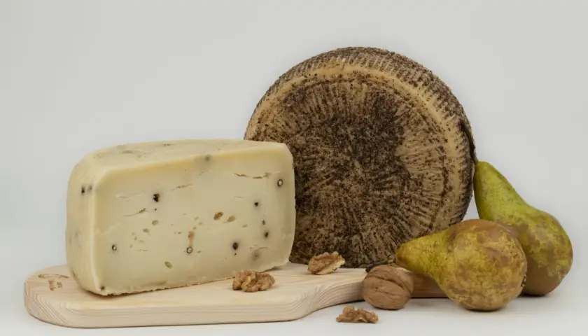 Varietà di tipi di pecorino, uno a spicchio con pepe nero, uno intero con crosta scura, pere e noci su tagliere di legno.