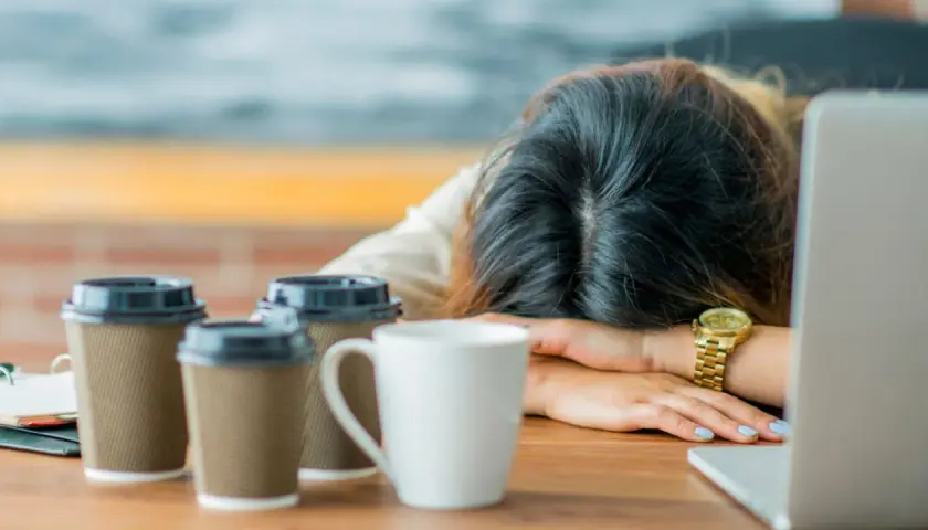 Erschöpfter Lehrer, Kopf auf dem Tisch, umgeben von Kaffeebechern. Die Anzeichen von **Lehrer Depression** sind deutlich.