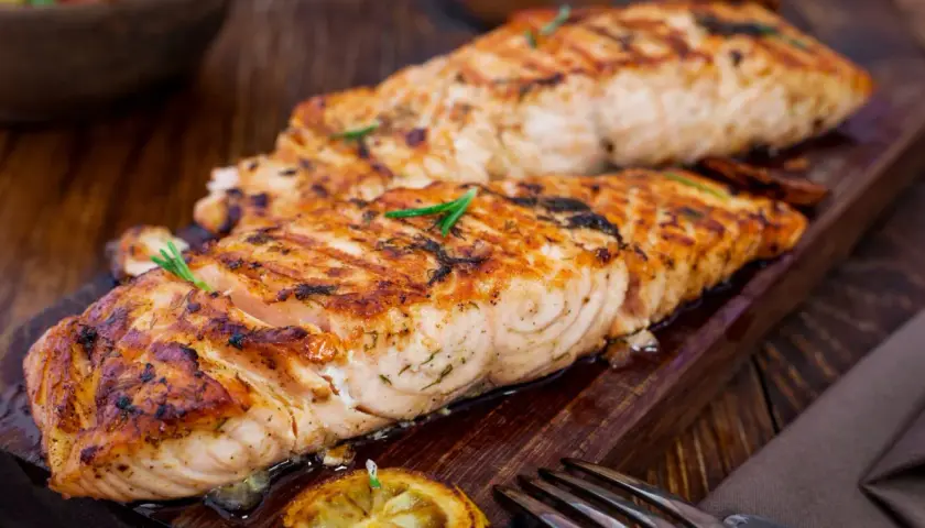 Två saftiga filéer av grillad fisk, perfekt kryddad med örter, serveras på en träbricka med citron och en gaffel.
